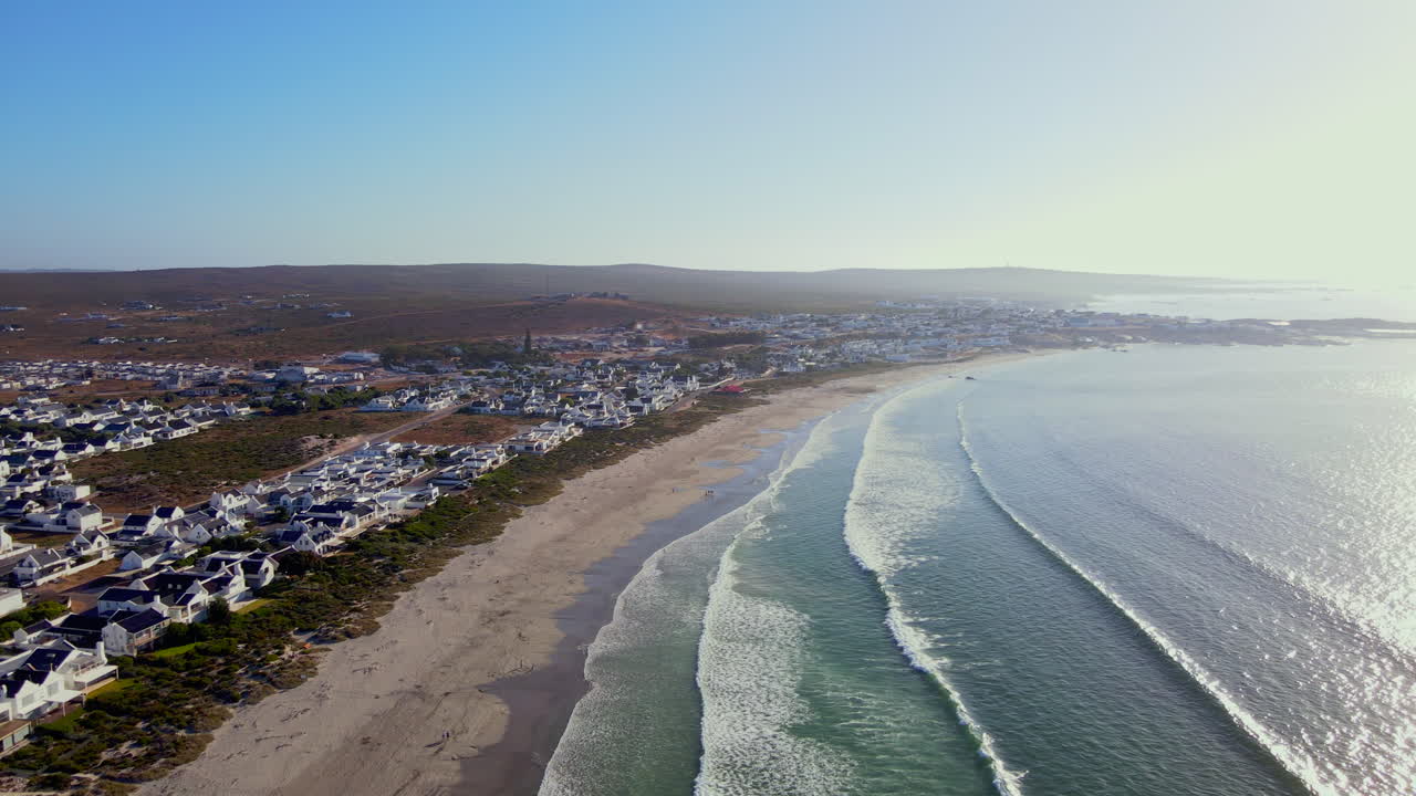 las olas rodan sobre una larga playa bordeada de casas blanqueadas, paternoster