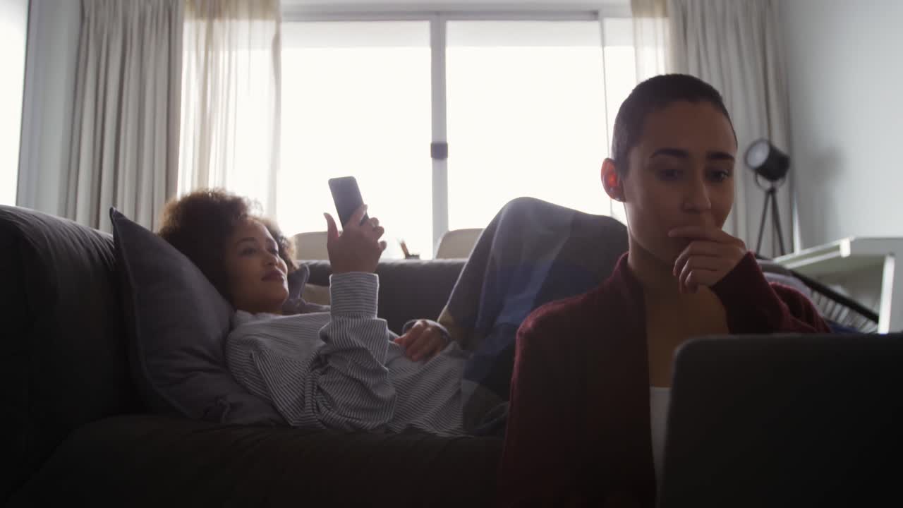 Lesbian couple using laptop and mobile phone in living room