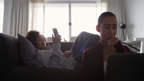 Lesbian-couple-using-laptop-and-mobile-phone-in-living-room