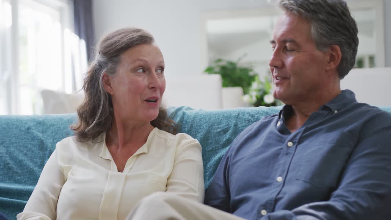 행복 한 고위 백인 커플 이 거실 에 앉아 이야기 하고 미소 짓고 있다