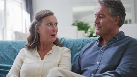 happy senior caucasian couple sitting in living room talking and smiling