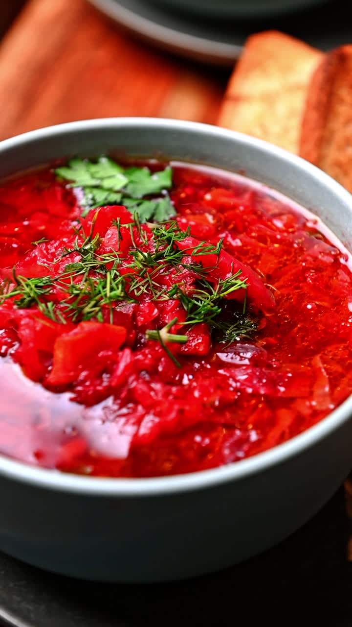 Traditional Ukrainian borscht with dill and parsley in ceramic bowl. Bright red borscht soup with beetroot and herbs served in bowl on gray plate with spoon