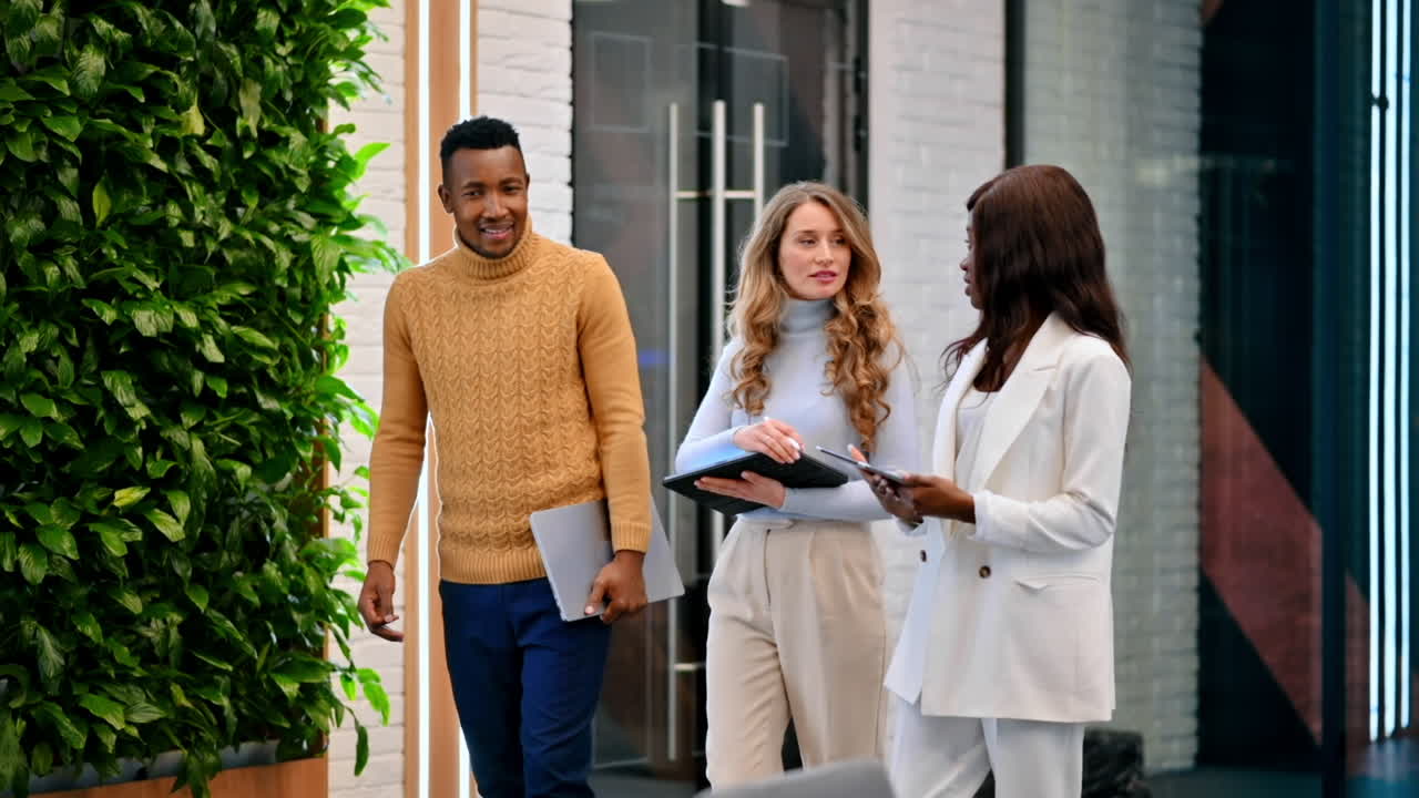 Multiracial group of workers walking in an office and discussing business affairs using tablets. Slow motion