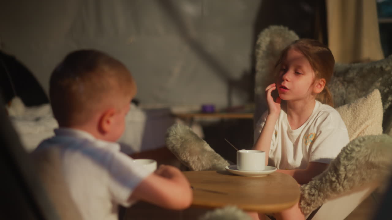 아이들은 집에서 따뜻한 음료를 마시며 대화를 나누고, 소녀는 테이블에서 소년과 이야기하고, 작은 형제와 여동생은 호텔 방에서 잠자리에 들기 전에 휴식을 취합니다.