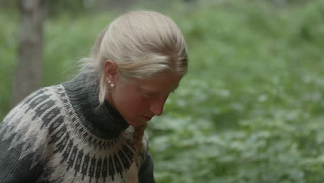 medium shot of a beautiful nordic blond girl picking stinging nettles with bare hands, urtica, in the finish forest, on the karhunkierros trail in the oulanka national park, finland