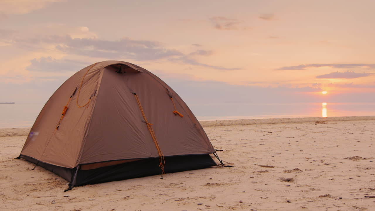 텐트는 주황색 바다와 일몰 배경의 모래에 있습니다.