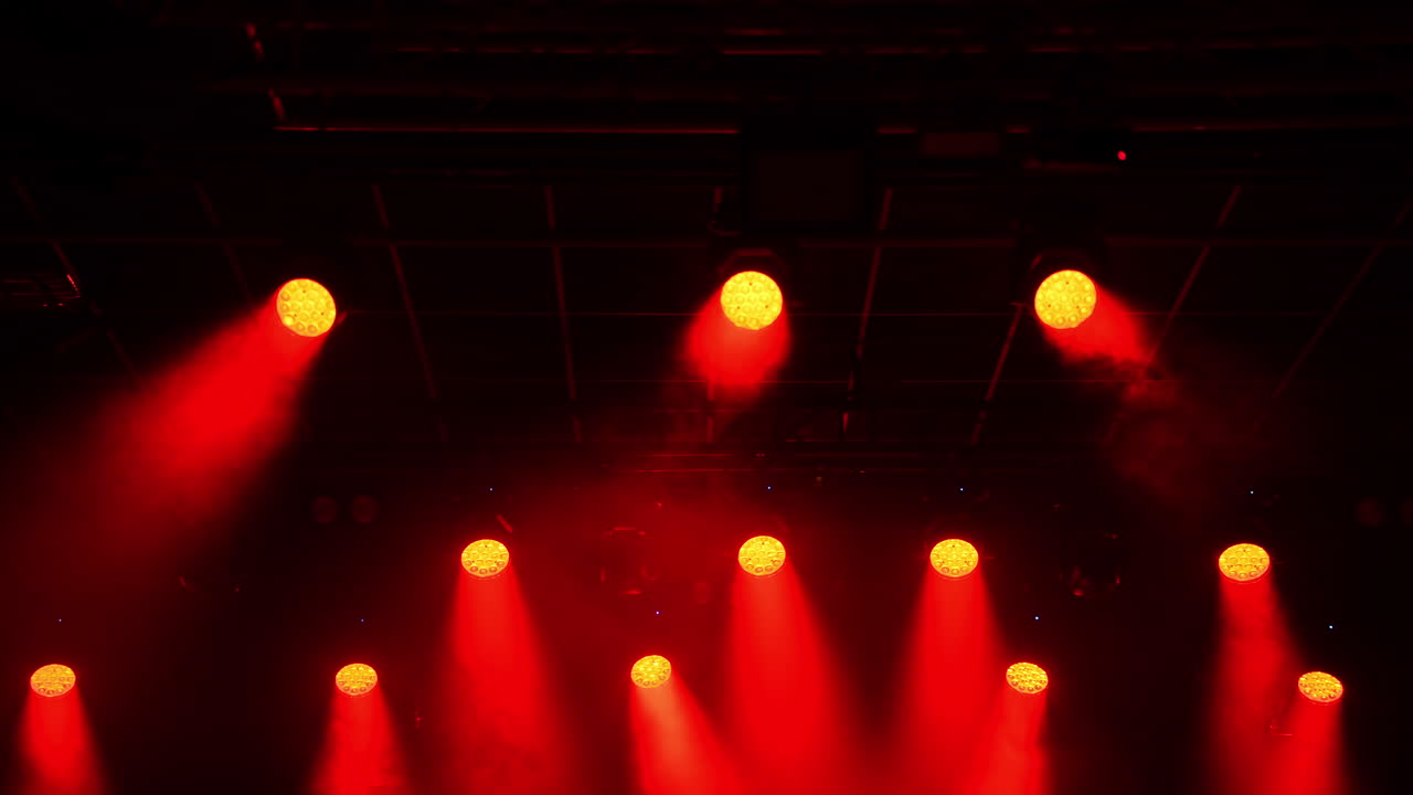 Metal grid hosting powerful red spotlights creating dramatic illumination, casting intense beams across dark concert hall staging area before upcoming performance