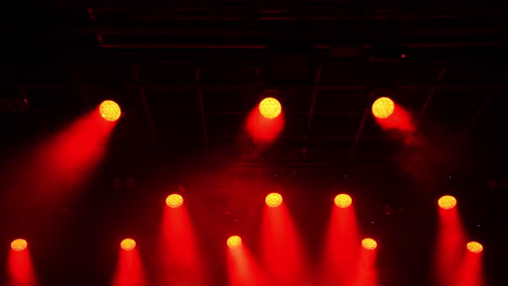 metal grid hosting powerful red spotlights creating dramatic illumination, casting intense beams across dark concert hall staging area before upcoming performance