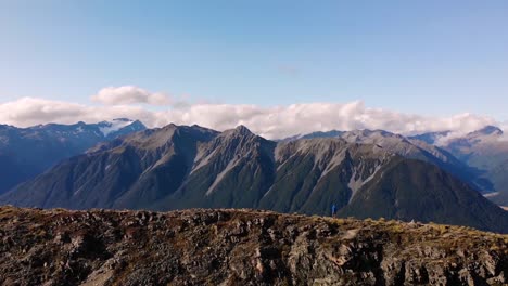 Un-Hombre-Valiente-Parado-En-Una-Cresta-Montañosa-Alta-Y-Estrecha-En-Los-Alpes-Del-Sur-Del-Paso-De-Arthur-En-Nueva-Zelanda---Panorámica-De-Disparos-De-Drones