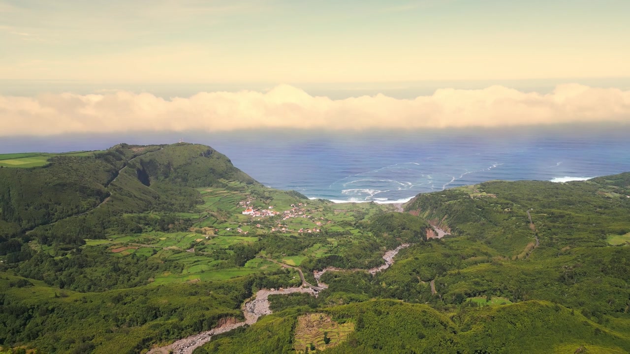Veduta aerea di un paesaggio verde lussureggiante e di una costa con un villaggio a Flores, Portogallo.