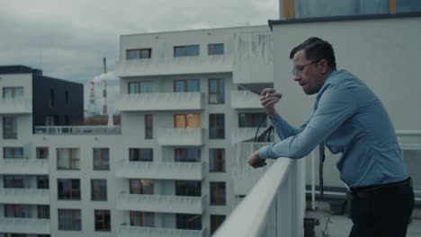 a sad man in a shirt smokes a cigarette on the balcony