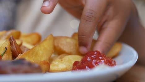 close-up of a child's hand reaching for a french fry on a plate of food