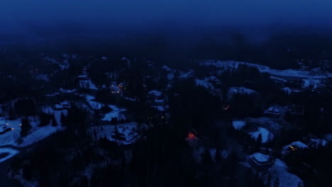 aerial drone backward moving shot over snow covered floor and houses beside frozen lakes after sunset