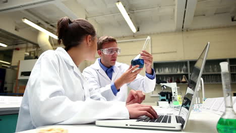 Focused-science-students-examining-chemical-and-using-laptop