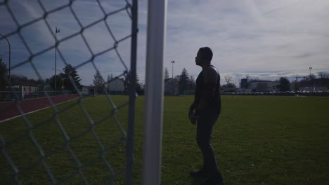 Male-Walking-Near-Fence-At-Dusk-With-Headphones-On---Strong-Athletic-Muscular-Black-Man-Fitness-Outdoor-Training-Preparation-In-4K