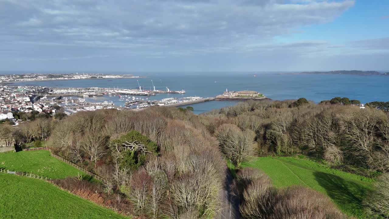 st. peter port guernsey vuelo desde la cima de val de terres sobre las cimas de los árboles hacia castle cornet con vistas sobre el puerto, los puertos deportivos, la bahía de belle greve y a través de herm