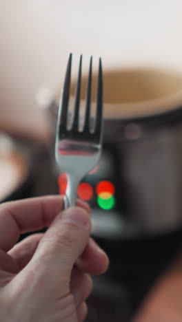 pov of a person holding a fork approaching a kitchen table with a multi-cooker blinking lights in the background, shot with a hand-held camera