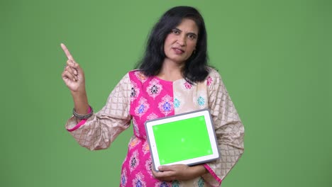 mature beautiful indian woman showing digital tablet and pointing finger up