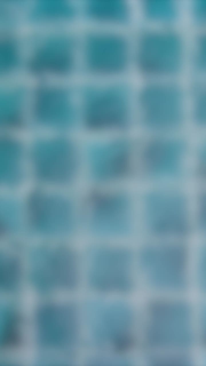 las gotas de lluvia crean ondas en una superficie de piscina azulejosa, capturadas en una secuencia de video serena y borrosa