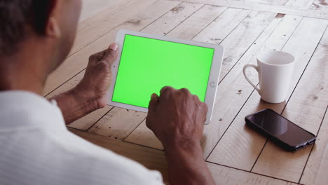 senior black man at a table using a tablet computer horizontally, over shoulder view, close up