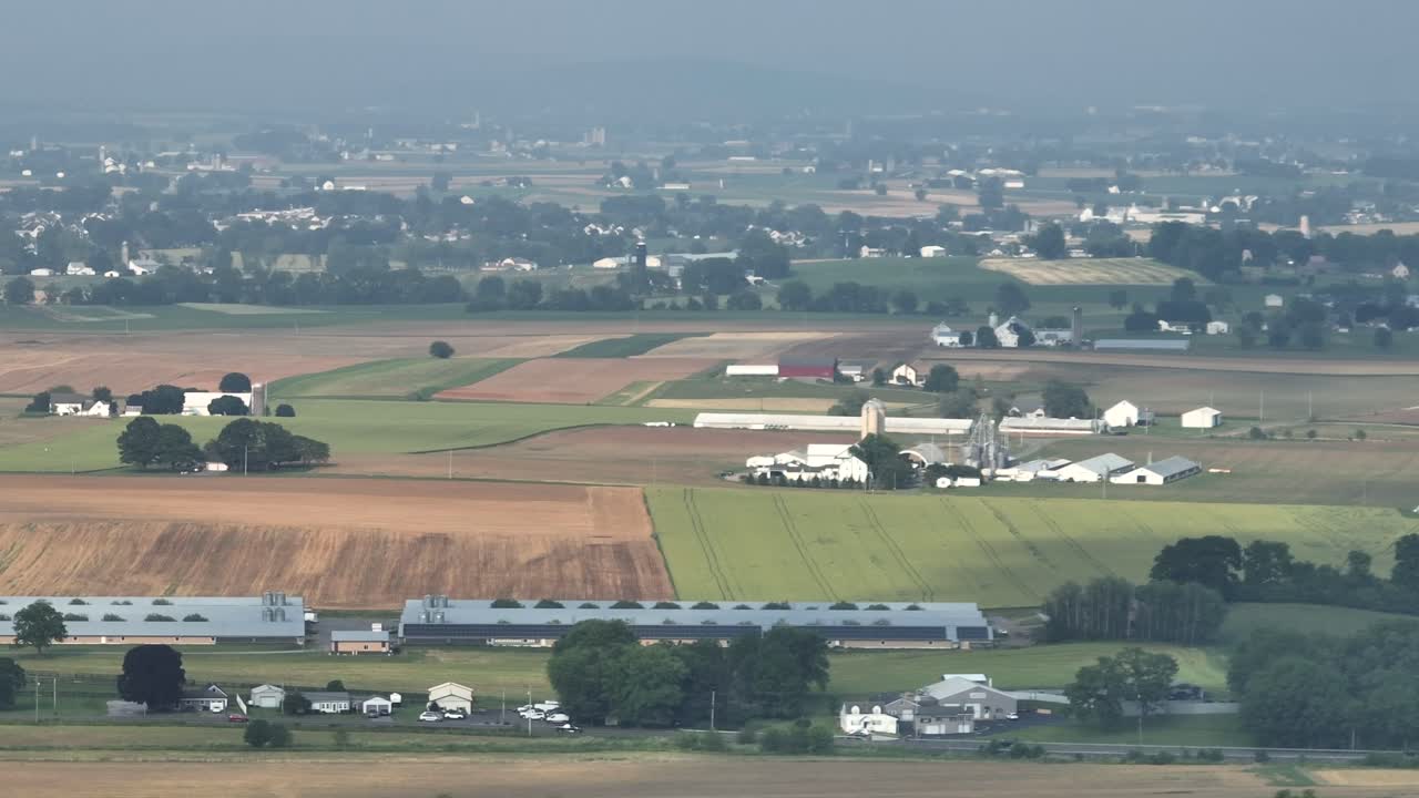 Aerial Tele wide angle shot of American farmsteads with barns and stables. Cloudy summer day in Midwest of USA. Panorama. Quiet scene with farm fields in countryside
