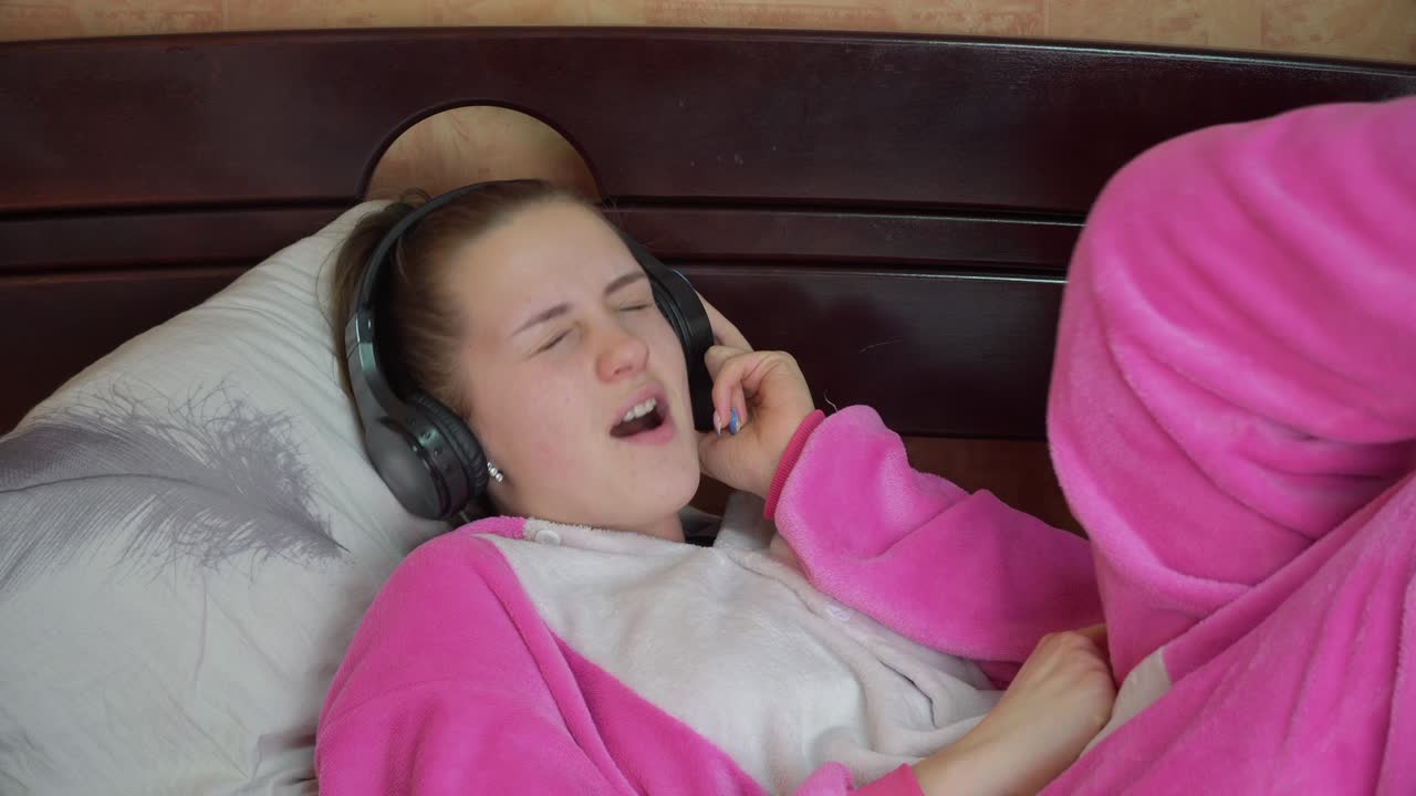 침대에 잠옷을 입은 소녀는 헤드폰을 통해 음악을 듣고 춤을 춘다