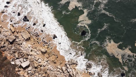 Sea-waves-crash-along-the-rocky-shoreline-of-Nazare,-Portugal,-a-destination-where-the-formidable-force-of-the-ocean-converges-with-the-varied-expanse-of-rocky-shores