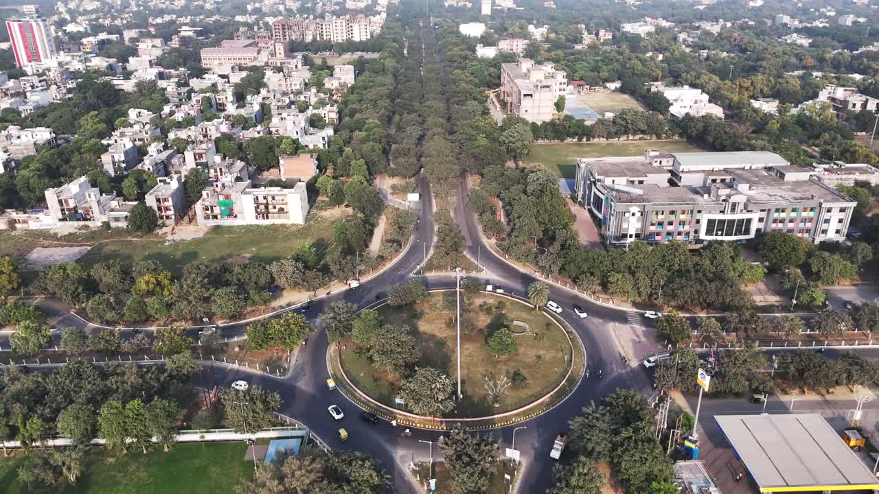 Vista aerea dall'alto di una rotonda di Greater Noida, che mostra strade radiali, veicoli in movimento e una fitta vegetazione, a simboleggiare una connettività efficiente all'interno di un paesaggio urbano pianificato