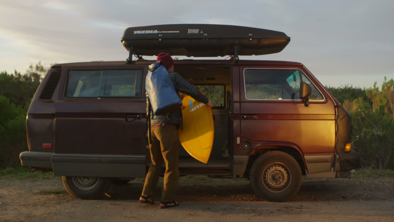 un sufrimiento saca su equipo de su autocaravana y se prepara para caminar hacia el surf en una zona costera