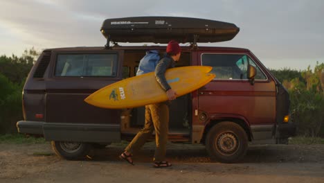 a suffer gets his gear out of his camper van and prepares to hike out to the surf in a coastal area