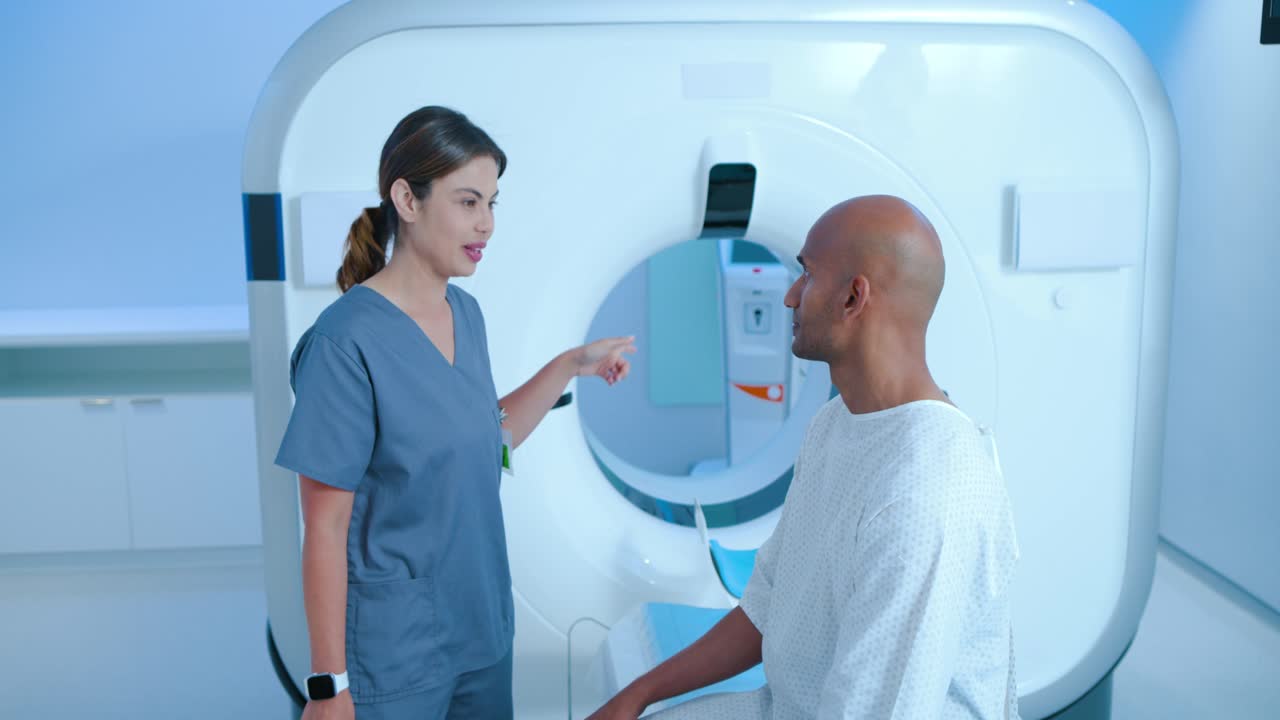 Tecnico radiologo donna che entra e appoggia la mano sulla spalla di un paziente uomo, indicando il gantry mentre si prepara per la scansione