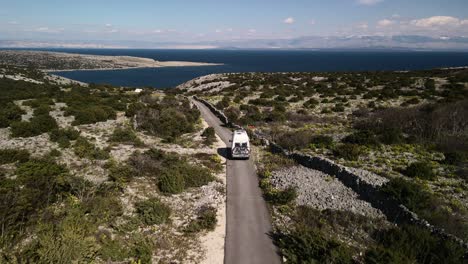 Einfacher-Gerader-Schuss-Mit-Drohne-Hinter-Einem-Wohnmobil-Mit-Geringer-Höhe,-Der-Das-Meer-Am-Blauen-Himmel-Des-Horizonts-Und-Das-Grün-In-Den-Bergen-Sonniger-Tag-4k-Beobachtet