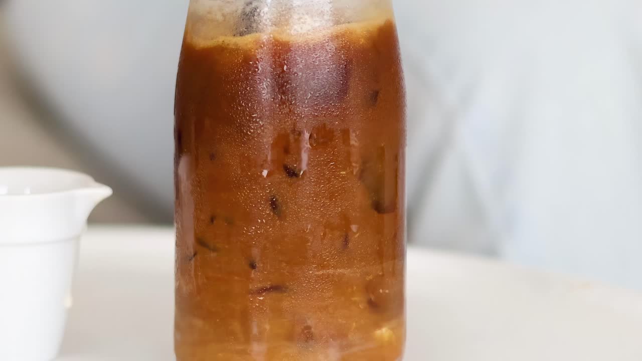 Watch as iced coffee blends with milk inside a glass bottle, creating a swirling effect.