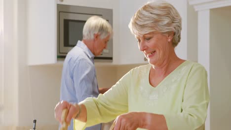 Senior-couple-talking-while-mixing-a-salad-in-kitchen