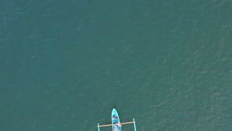 a small traditional local boat appears on the warm calm tropical waters of bali, aerial god view