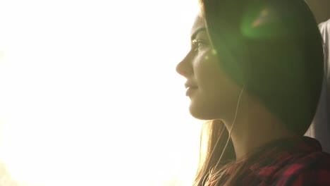 side view of a beautiful caucasian girl going somewhere by train. listen music in earphones. pensive female. smiling. sun shines