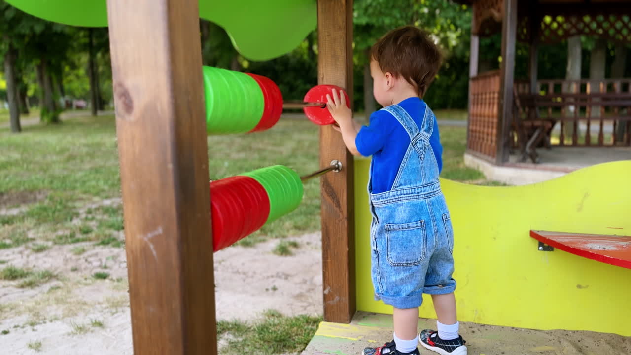 Beautiful Caucasian baby boy playing with abacus on the playground. Toddler spending time outdoors in summer.