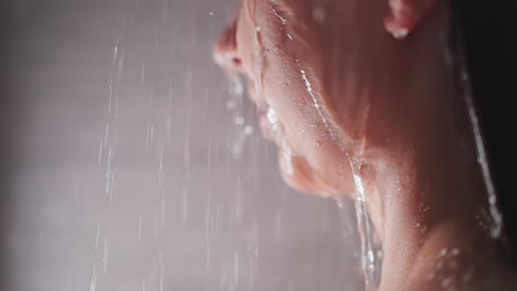 happy woman with water pouring on face in bathroom closeup. smiling lady takes relaxing shower in home washroom. reducing stress with spa care