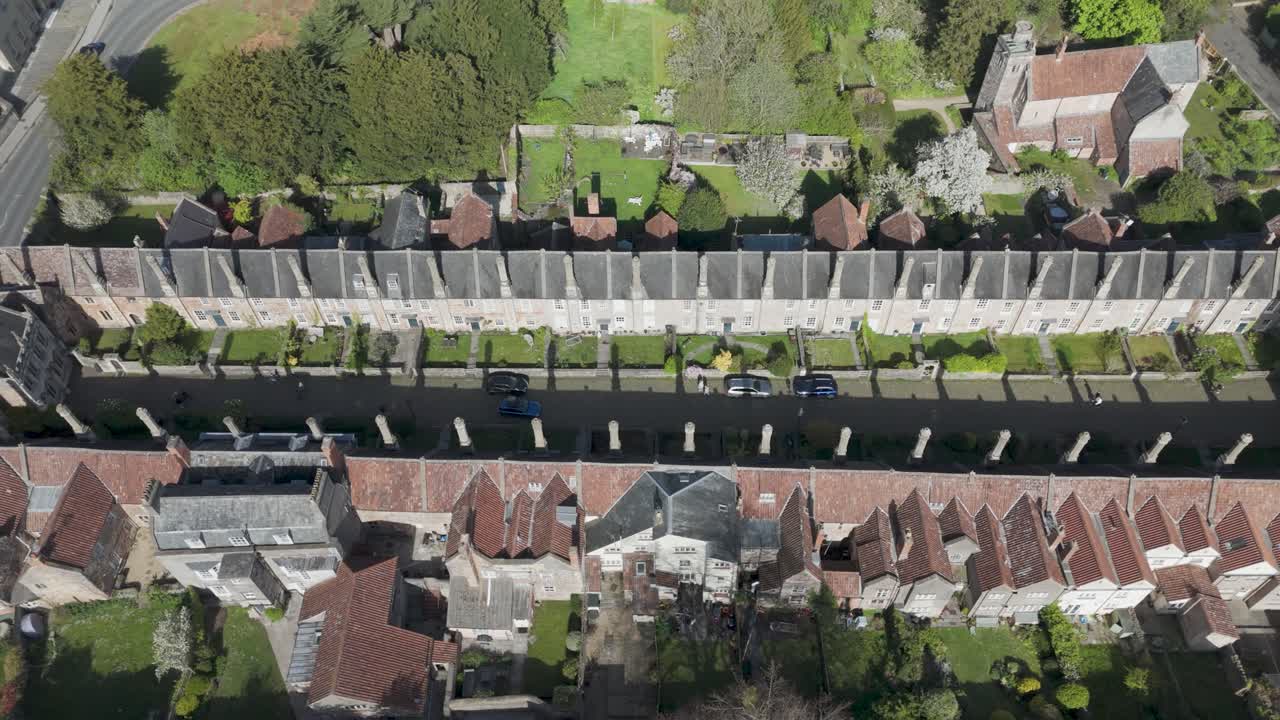 Aerial orbit of medieval Vicars’ Close showing uniform stone terrace, tall chimneys and cobbled lane aligned toward Wells Cathedral, exemplifying preserved heritage streetscape and historic living