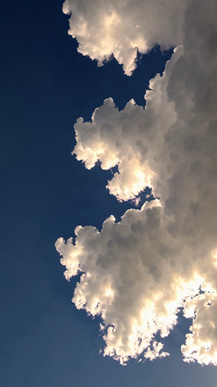 A dramatic upward angle captures fluffy clouds against a deep blue sky, creating a serene