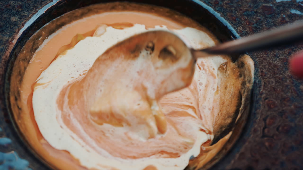 Close up of a gourmet soup topped with light foam and garnishes, served in a rustic ceramic bowl