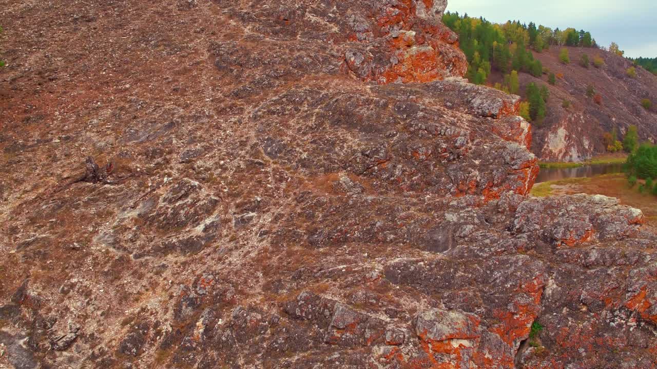 una gran roca naranja se eleva por encima de la superficie del agua. dos abetos verdes brillantes crecen en el suelo rocoso. fotografía aérea.