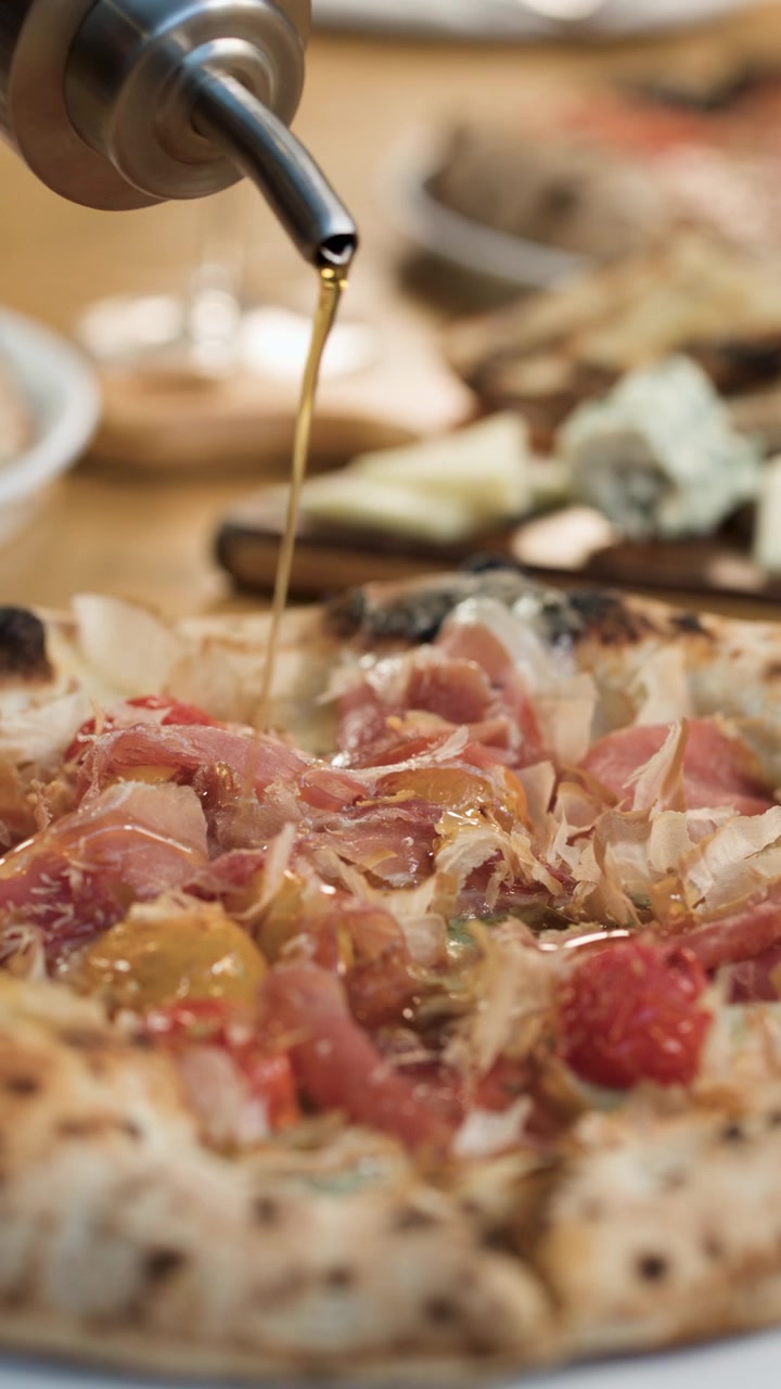 Primo piano di olio d'oliva che cola su una pizza gourmet al prosciutto in un ristorante italiano