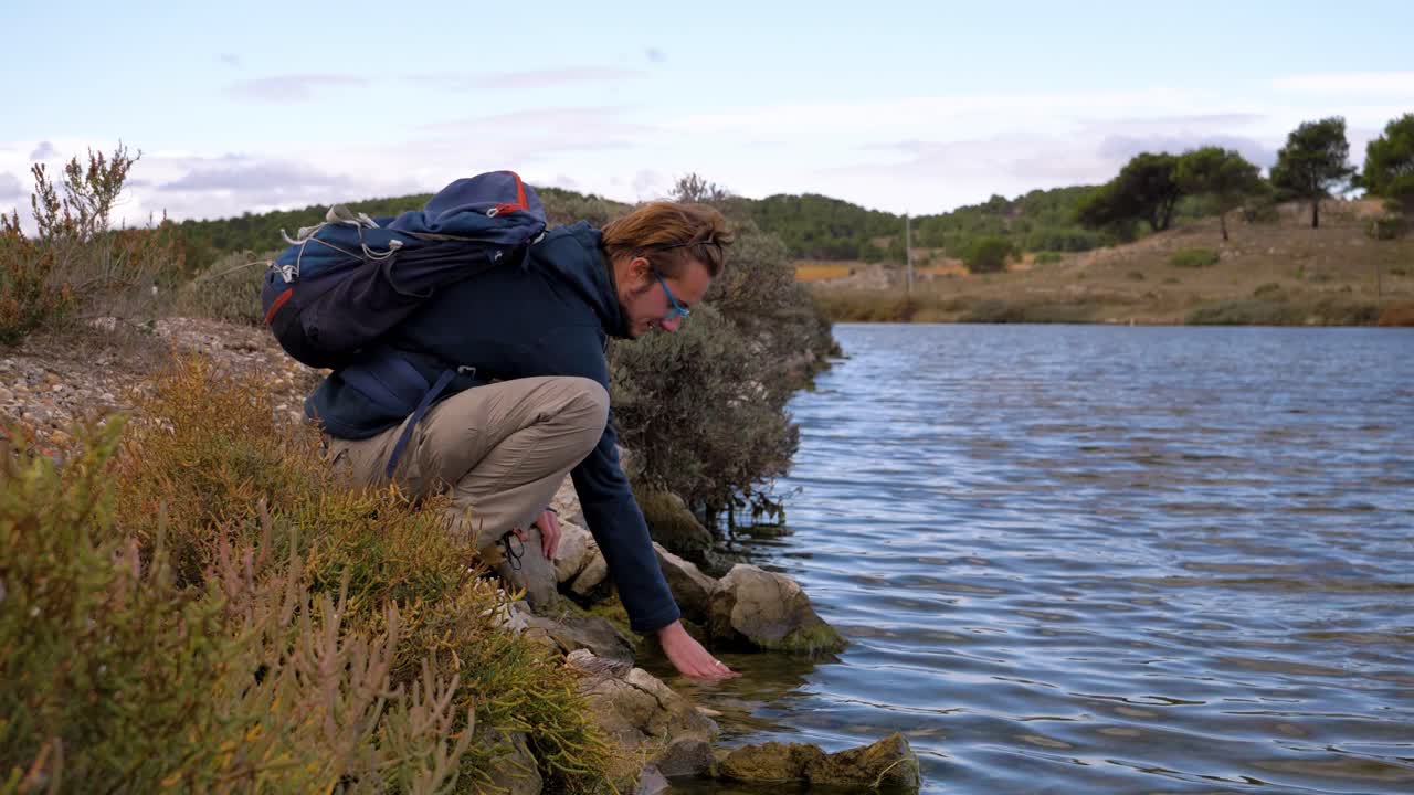 медленный снимок человека, присевшего у берега озера, чувствующего температуру.