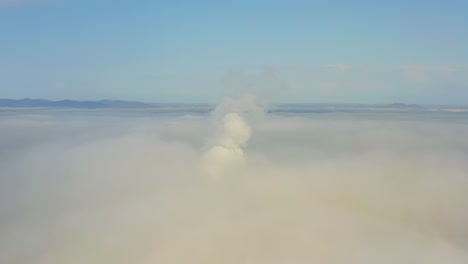 smoke from a power station chimney rising from a low, creeping fog. drone view