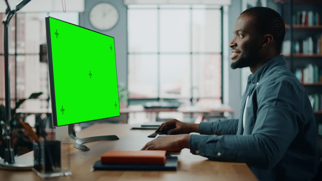 Handsome Black African American Specialist Working on Desktop Computer with Green Screen Mock Up Display at Home Living Room. Freelance Man Chatting to Clients Over the Internet on Social Networks.