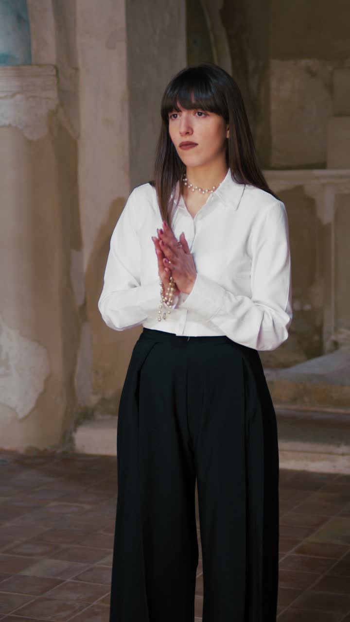 Giovane donna devota in piedi in chiesa che prega con le mani giunte