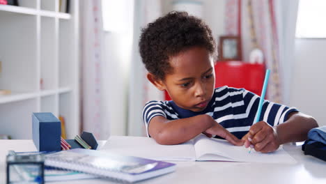 young boy sitting at desk in bedroom and drawing
