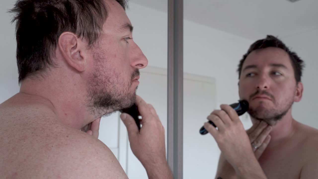 전기면도기로 거울 앞에서 수염을 면도하는 남자