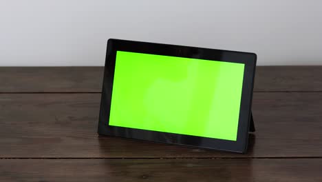 a tablet with a green screen on a wooden table, makes a doubletap with a finger.